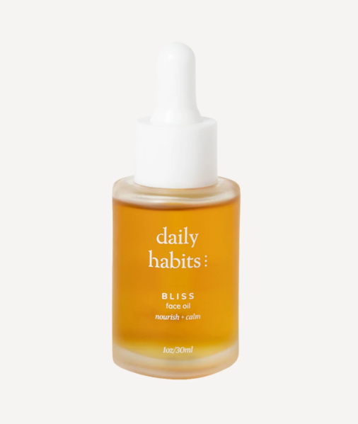 Orange bottle of 'daily habits' face oil with a white dropper on a light beige background