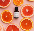 Bottle of 'essence one' essential oil blend surrounded by sliced oranges and grapefruits on a pink background